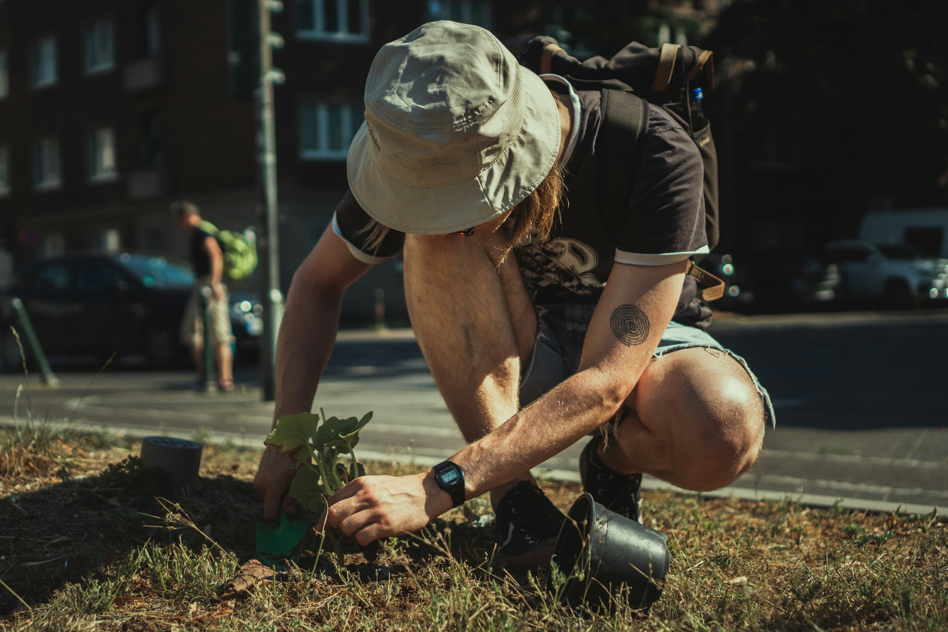 A man in a bucket hat planting a tree in an urban setting