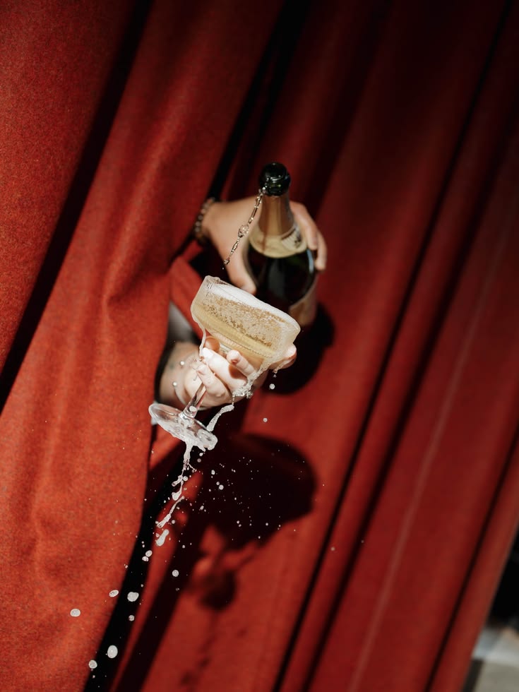 Red velvet curtain with hand pouring champagne into glass